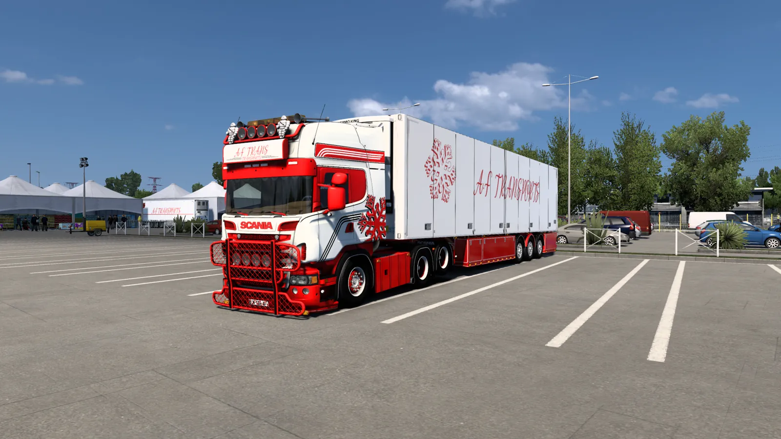 Un Scania R blanc et rouge attelé à une remorque frigorifique AF Transports, sur une aire dégagée